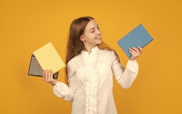 Niño alegre que muestra el libro escolar sobre fondo amarillo de regreso a la escuela