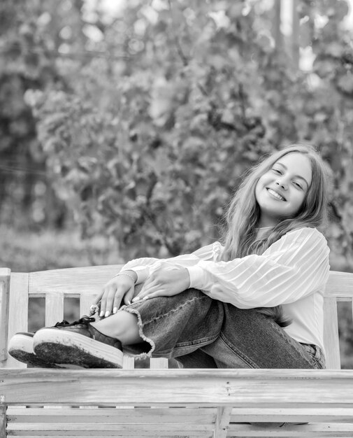 Un niño alegre se sienta en un banco para relajarse al aire libre