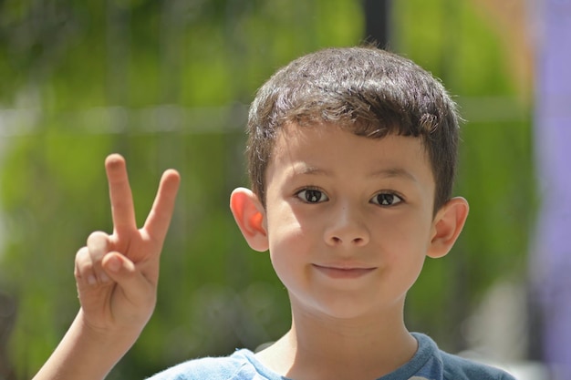 Niño alegre con el signo de la paz y el amor en un enfoque selectivo de fondo verde borroso