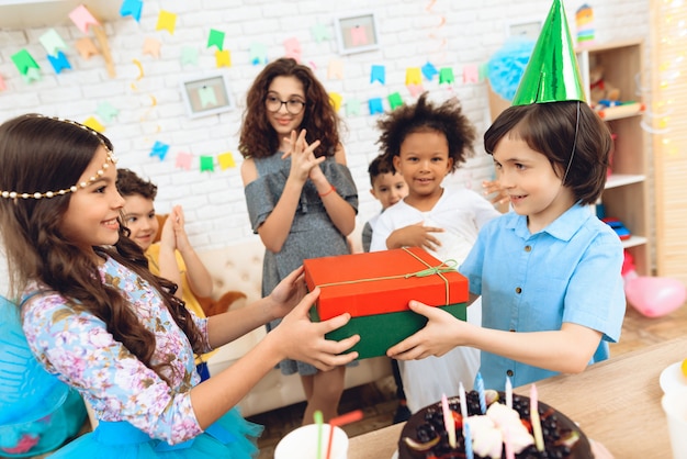 Foto niño alegre en sombrero festivo recibe regalo de niña.