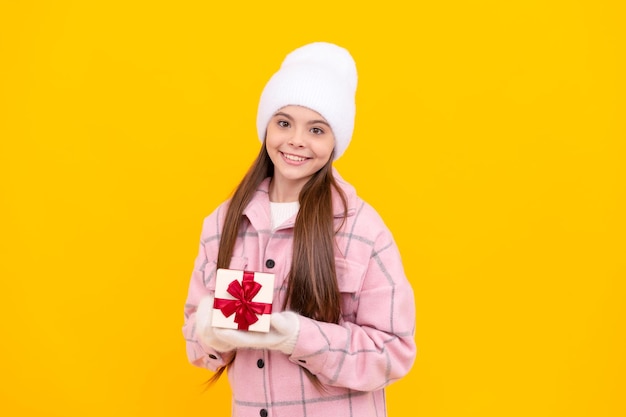 Niño alegre con sombrero y mitones sostiene caja de regalo sobre fondo amarillo navidad