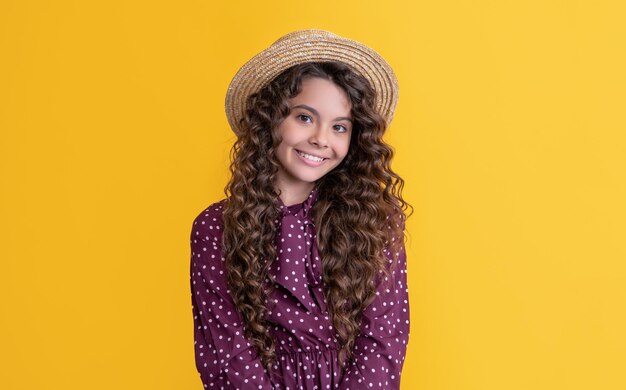 Niño alegre con sombrero de paja con cabello largo y rizado moreno sobre fondo amarillo