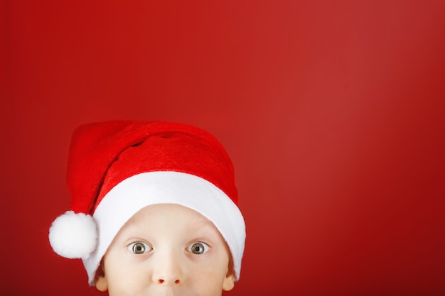 Niño alegre con un sombrero de Santa mira desde la parte inferior del marco