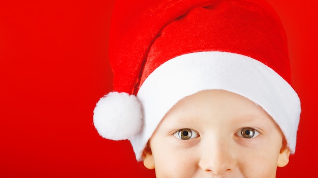 Niño alegre en un sombrero de Santa sobre un fondo rojo se asoma desde la parte inferior del marco
