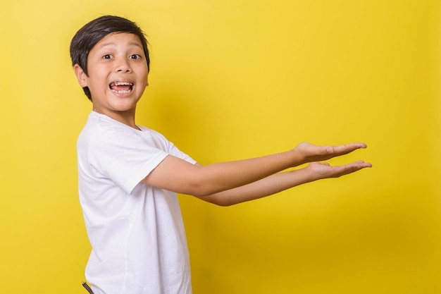 Niño alegre sonriendo con gesto de presentación lateral aislado sobre fondo amarillo