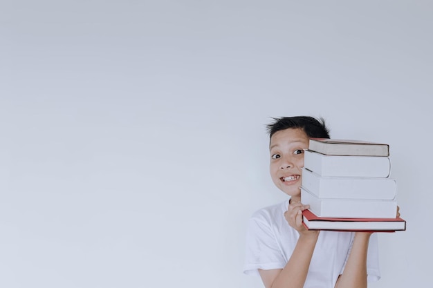 Niño alegre sosteniendo un montón de libros con espacio de copia aislado en fondo blanco