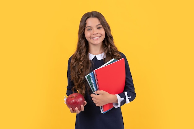 Niño alegre sostiene cuadernos escolares para la tarea y almuerzo de manzana en el almuerzo de fondo amarillo