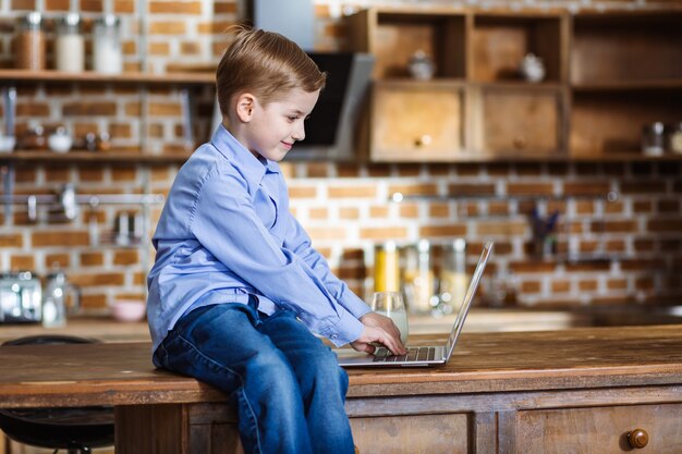 Niño alegre usando su computadora portátil mientras está sentado en la mesa