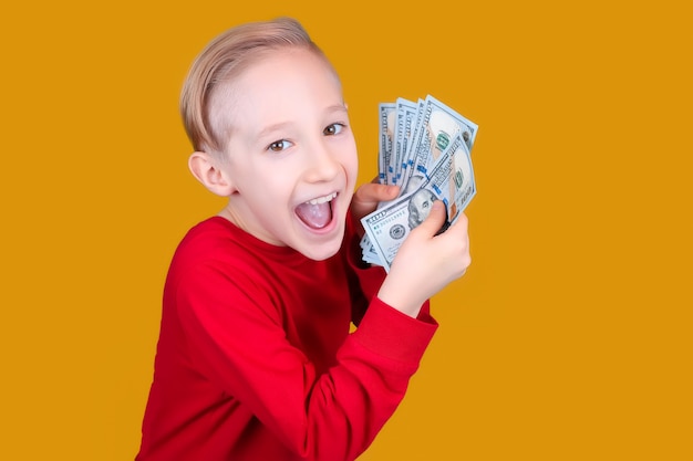 Un niño alegre vestido de rojo sostiene un fajo de billetes de dólar frente a él y hace muecas