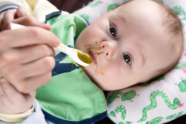 El niño, alimentándose de la primera cuchara, prueba las verduras por primera vez, las emociones.