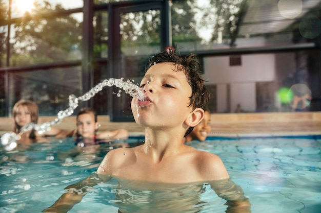 niño, con, amigos, en, piscina cubierta, escupir, agua