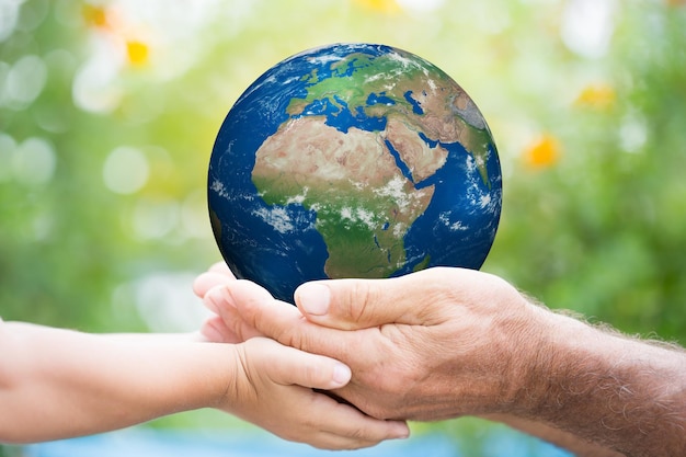 Niño y anciano sosteniendo el planeta Tierra en las manos contra el fondo verde de la primavera Elementos de esta imagen proporcionados por la NASA