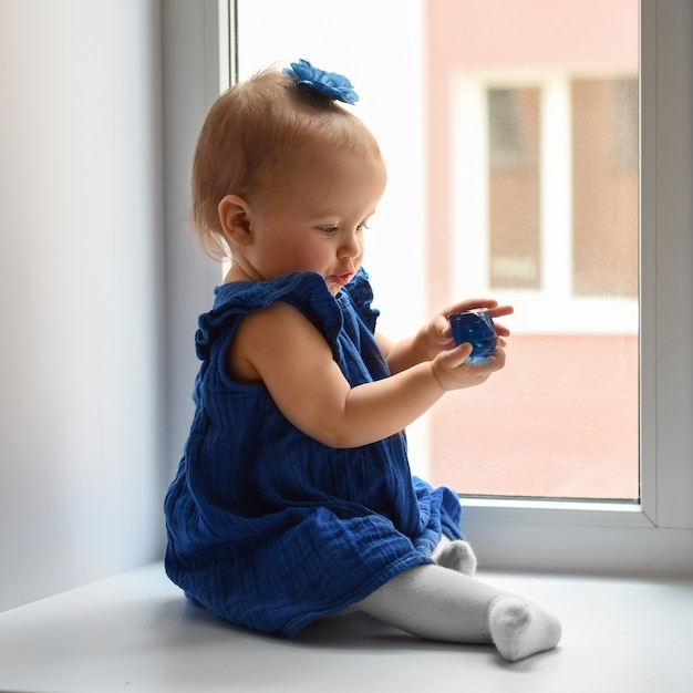 Foto un niño de un año bebé una niña con un vestido azul en la ventana