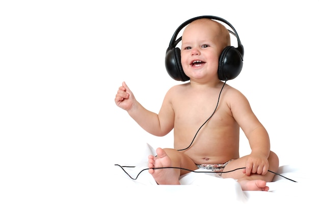 Niño de un año escucha música en grandes auriculares y sonríe sobre un fondo blanco aislado
