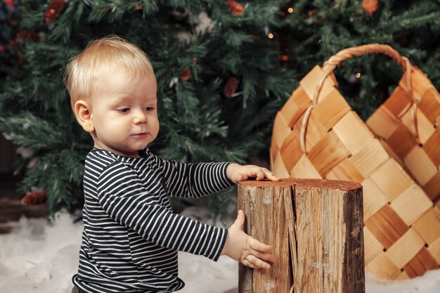 Niño de un año en una manta mullida blanca jugando por el árbol de Navidad. Chico lindo en la sala de estar decorada de Navidad. Niño pequeño mirando a otro lado. Concepto de niños feliz año nuevo. Copie el espacio para el sitio