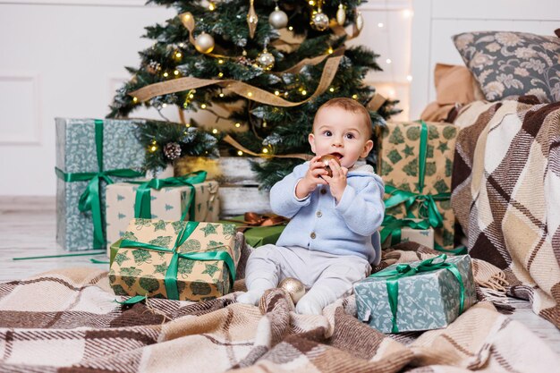 Un niño de un año se sienta cerca de un árbol de Navidad decorado con regalos Árbol de Navidad en la casa Un niño feliz está esperando el nuevo año