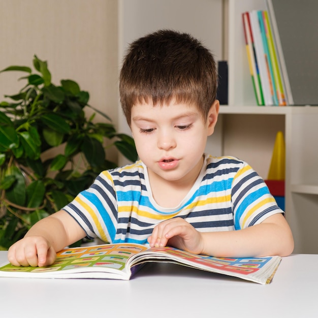 Un niño de un año se sienta en una mesa y lee un libro.