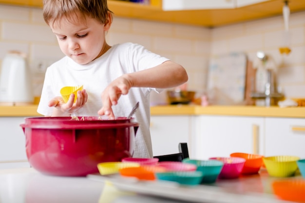 Un niño de años cocina cupcakes en una cocina ligera en casa, un niño usa moldes de silicona para hornear