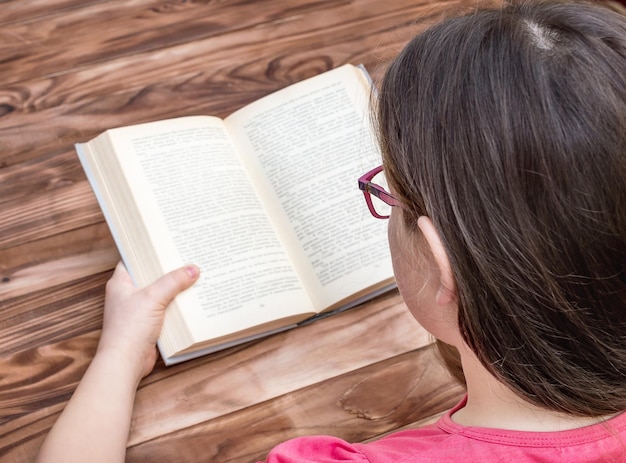 Foto niño con anteojos leyendo un libro sobre la mesa