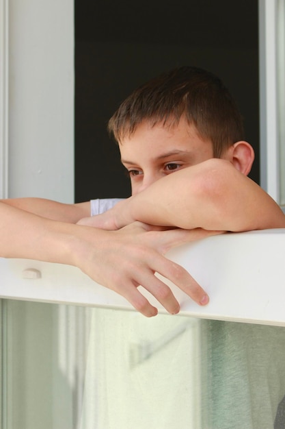 Foto un niño está apoyado en un alféizar de la ventana y mirando hacia afuera