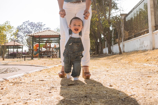 El niño aprende a caminar sosteniendo las manos de su madre al aire libre