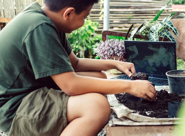 Niño aprende a cultivar flores en macetas a través de la enseñanza en línea de palear tierra en macetas para preparar plantas