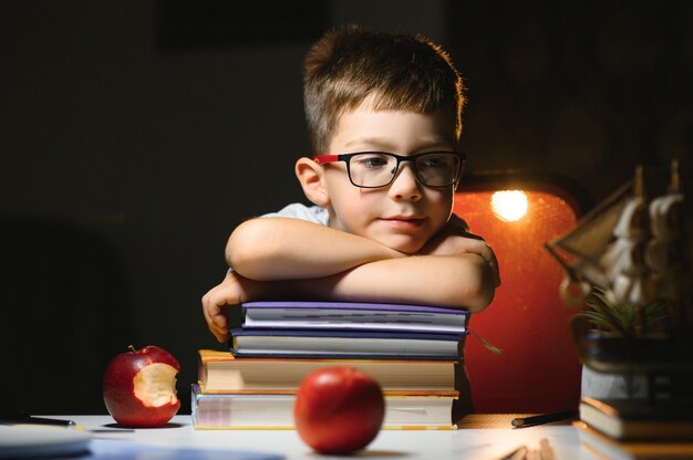 Niño aprende lecciones en el hogar en la mesa a la luz de una lámpara de mesa.