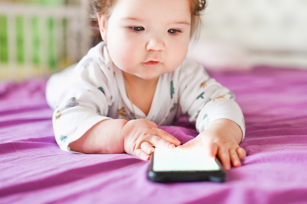 El niño aprende por teléfono móvil. Pequeño bebé recién nacido que alcanza para un teléfono móvil