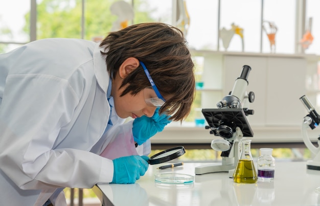 Niño aprendiendo y mirando a través de una lupa a productos químicos en un laboratorio de aula