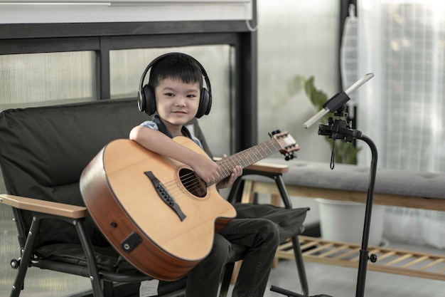 Un niño aprendiendo a tocar la guitarra, Concentrado en tocar la música, un niño pequeño practicando un nuevo sonido con una guitarra en casa, un niño divirtiéndose haciendo música con la guitarra y cantando en casa.
