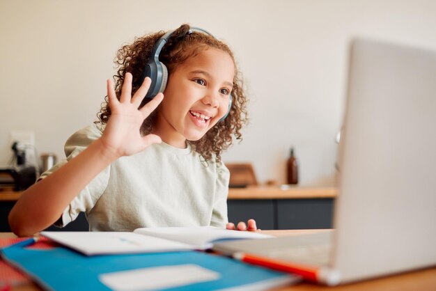 Niño de aprendizaje a distancia en línea en la cámara web de la computadora portátil o videollamada que se une a la lección con auriculares y saludo de saludo o gesto de despedida Pequeño estudiante feliz en un aula remota con un cuaderno de enseñanza