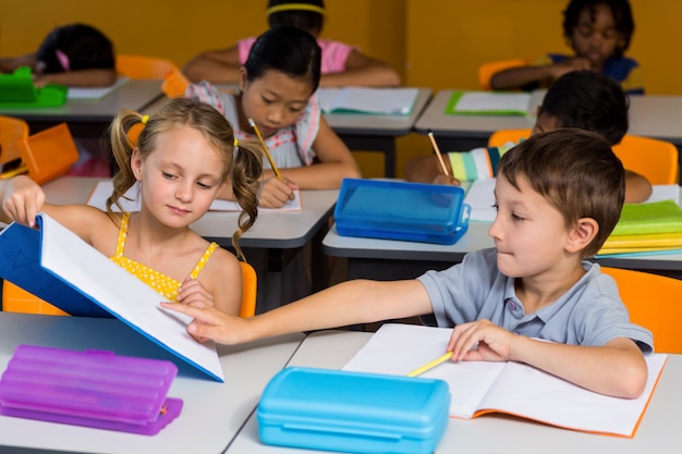 Niño apuntando al libro mostrado por compañero de clase