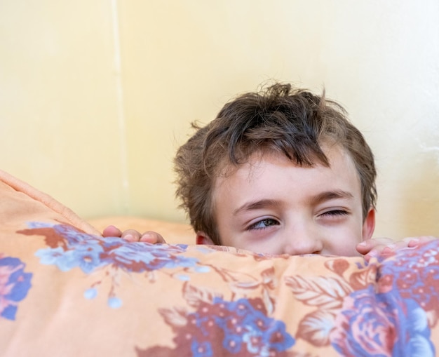 Niño árabe jugando al escondite y escondiéndose detrás de un cojín