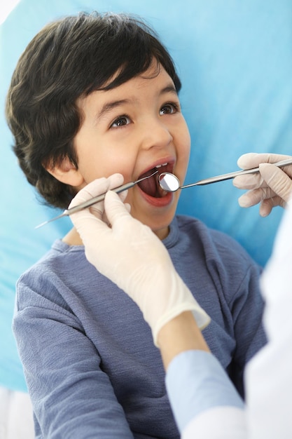 Niño árabe sentado en el sillón dental con la boca abierta durante el chequeo oral mientras el médico visita el consultorio del dentista Concepto de medicina y estomatología