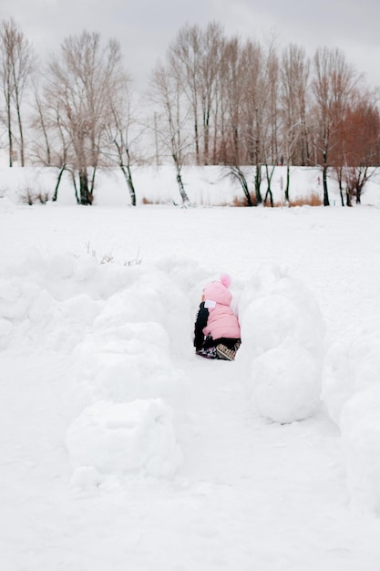 Niño arrastrándose en la nieve acumulada en invierno en el parque vistiendo ropa de abrigo de invierno asombroso fondo lleno...