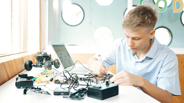 Niño arreglando la placa principal mientras estudia construcción usando la edificación de la computadora portátil