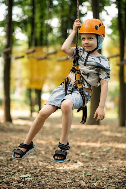 Un niño en un aseguramiento de montaña y una chancleta atraviesa una carrera de obstáculos. Actividad activa y deportiva en verano para un niño.