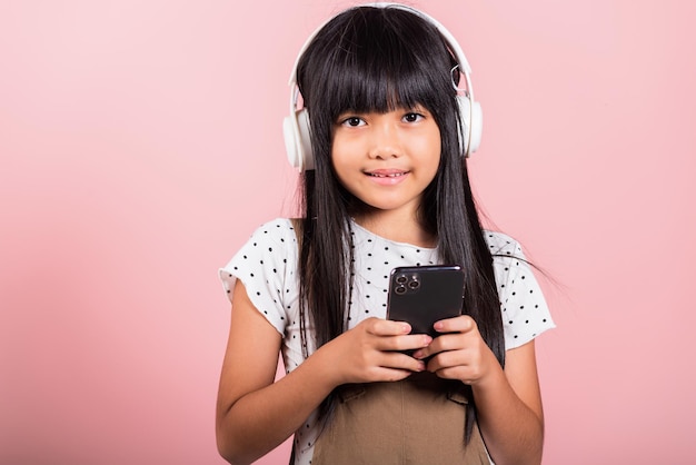 Niño asiático de 10 años disfrutando de escuchar música desde el teléfono móvil usando auriculares inalámbricos