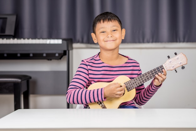 Un niño asiático de entre 7 y 8 años. Juega un ukelele en la habitación, amor apasionado en la música.