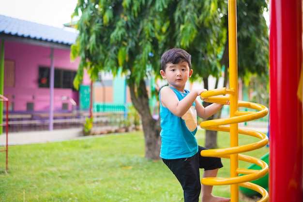 Niño asiático activo que juega el espiral del metal que sube en el patio del patio de la escuela.