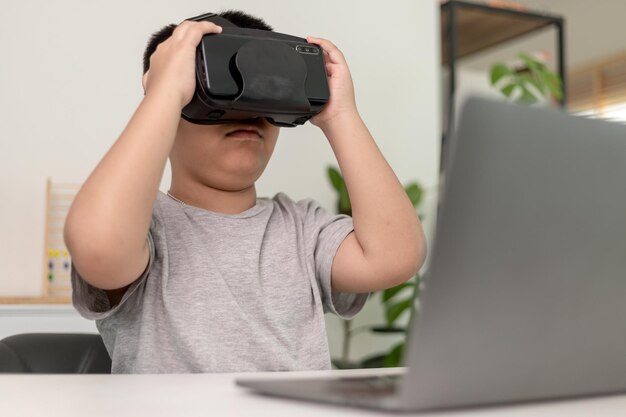 Un niño asiático con anteojos VR que estudia ciencias en casa, un estudiante curioso usa un auricular de realidad virtual para estudiar ciencias en casa, estudiar en línea, aprender un estilo de vida futurista