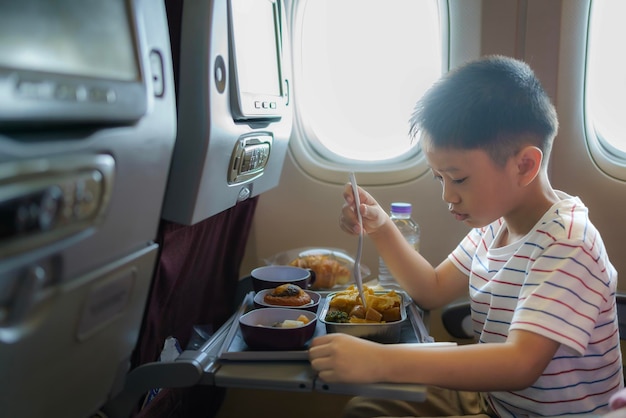 Niño asiático en el asiento de la ventana del avión Menú especial de vuelo para niños