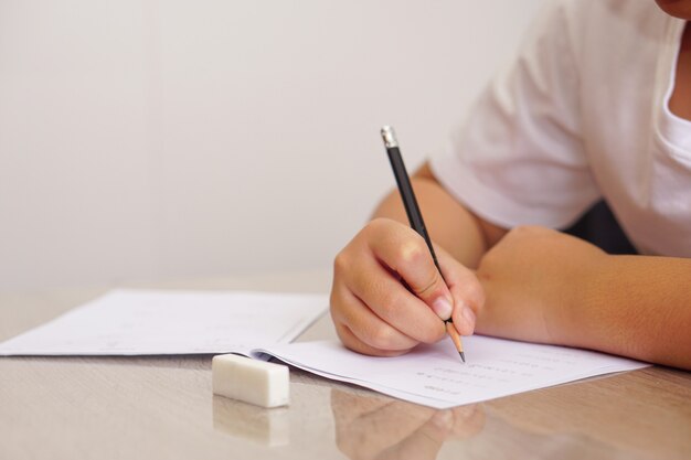 Un niño asiático con una camiseta blanca haciendo los deberes o escribiendo un cuaderno con lápiz sobre la mesa. Concepto de educación y aprendizaje.