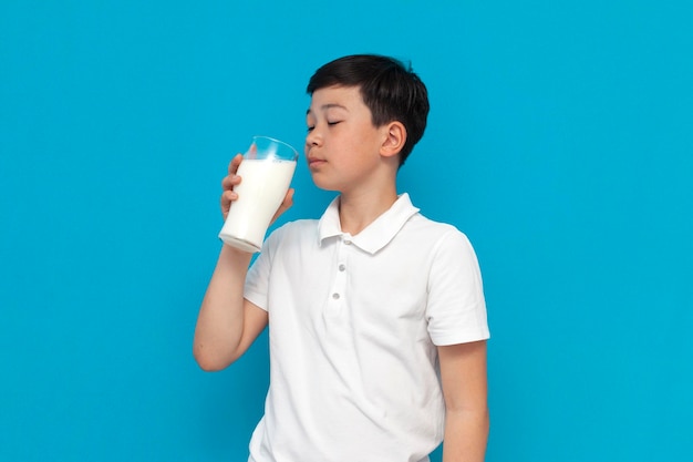 Un niño asiático con una camiseta blanca sostiene un vaso de leche con un niño coreano de fondo azul.