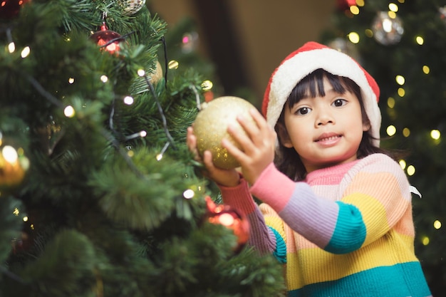 Niño asiático colgando una bola de juguete decorativa en la rama de un árbol de Navidad