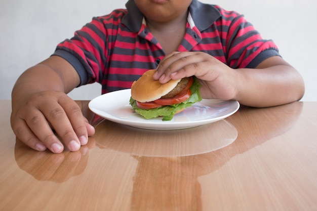 Niño asiático come una hamburguesa, comida chatarra poco saludable para niños