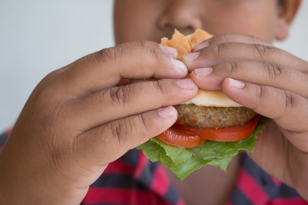 Niño asiático come una hamburguesa, comida chatarra poco saludable para niños