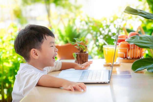 Foto niño asiático divertido y viendo dibujos animados video en él computadora cuaderno en la mesa en el jardín de la casa