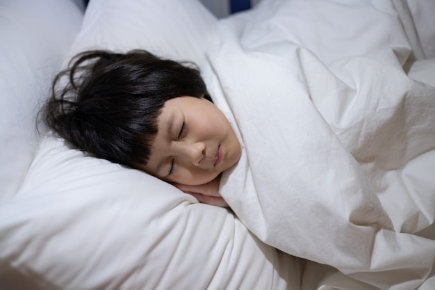 niño asiático dormir en la cama, niño enfermo