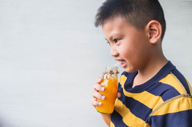 Un niño asiático está bebiendo una botella de jugo de naranja.